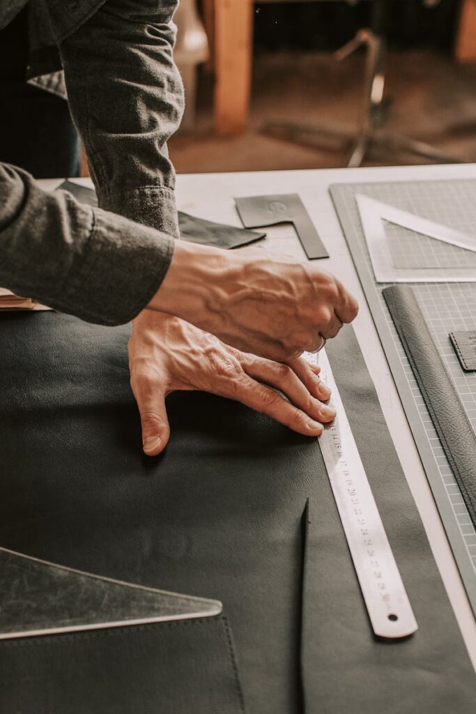 Close-up of hands working on leather crafting with tools in a workshop setting.